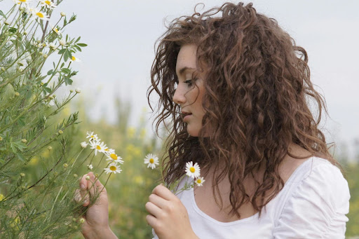 redhead girl in flower field holding and enjoying the smell of flowers