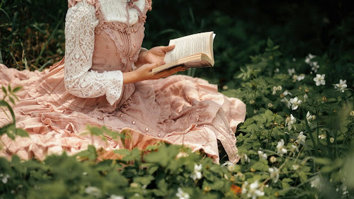 woman reading in a meadow of flowers wearing a girly dress