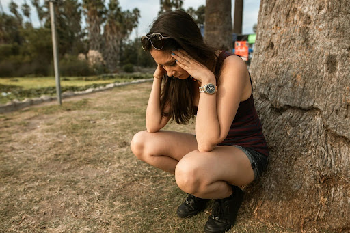 woman stressed holding head in hands squatting by a tree